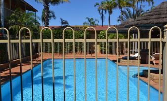 a large swimming pool surrounded by a wooden fence , with palm trees in the background at The Lodge Motel