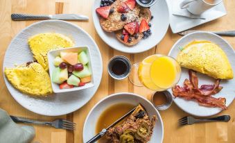 a table is set with plates of breakfast food , including pancakes and fruit , as well as cups of coffee at Cambria Hotel West Orange