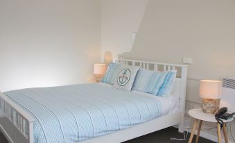 a white bed with a blue comforter and pillows , along with a nightstand and lamp in the corner at Beauty Point Waterfront Hotel