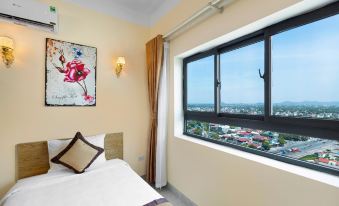 a bedroom with a large window offering a view of the city , featuring a bed and a painting on the wall at Tien Loc Palace Hotel