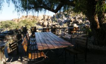 an outdoor dining area with a wooden table surrounded by chairs , surrounded by rocks and trees at Canyon Lodge