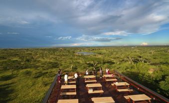 a group of people standing on a rooftop terrace overlooking a vast , open landscape with trees and water at Seronera Wildlife Lodge