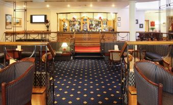 a bar with wooden chairs and tables , a blue carpet , and a red carpeted area at Mercure York Fairfield Manor Hotel
