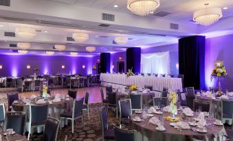 a large banquet hall with multiple dining tables , each set for a special occasion , and purple lighting at DoubleTree by Hilton Hotel Syracuse