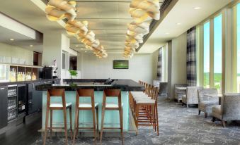 a modern bar with a marble counter and wooden chairs , surrounded by large windows and chandeliers at DoubleTree by Hilton Cedar Rapids Convention Complex