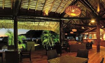 a tropical dining area with thatched roofs , wooden furniture , and tropical plants under a hanging light at Nanuya Island Resort