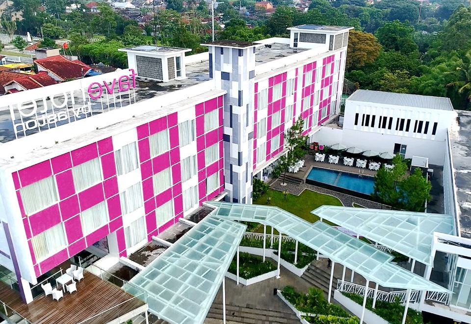 a tall building with a pink and white facade is surrounded by a glass walkway at Favehotel Cimanuk Garut