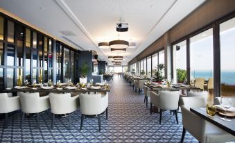 a large , well - lit dining room with multiple tables and chairs , all facing a sky view at Divan Mersin