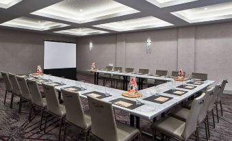 a conference room with a long table and chairs , a projection screen on the wall , and framed pictures at The Del Monte Lodge Renaissance Rochester Hotel & Spa