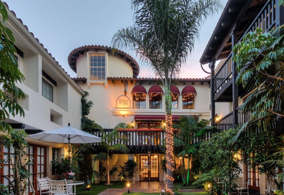 a building with a red awning and palm trees in the foreground , while a white house and patio area are visible in the background at Best Western Plus Carpinteria Inn