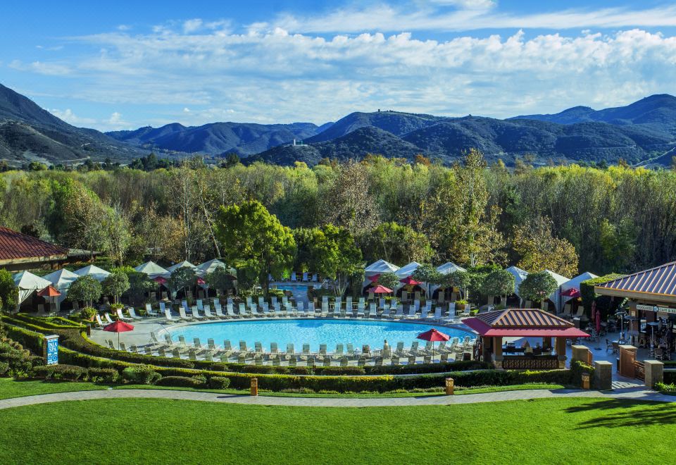 a large outdoor pool surrounded by lounge chairs and umbrellas , with a view of the mountains in the background at Pala Casino Spa and Resort