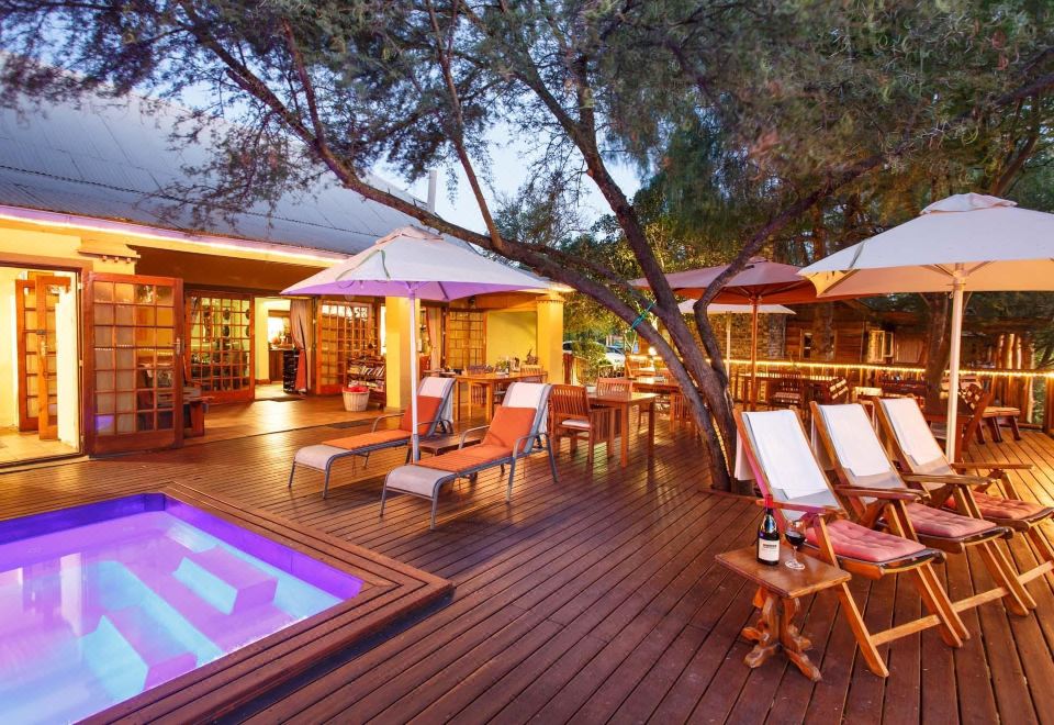 a large wooden deck with chairs and umbrellas , surrounded by trees and a pool , creating a relaxing atmosphere at Riverside Guest Lodge