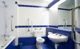 a blue and white bathroom with a toilet , sink , and shower , as well as a mirror above the sink at Travelodge Kendal