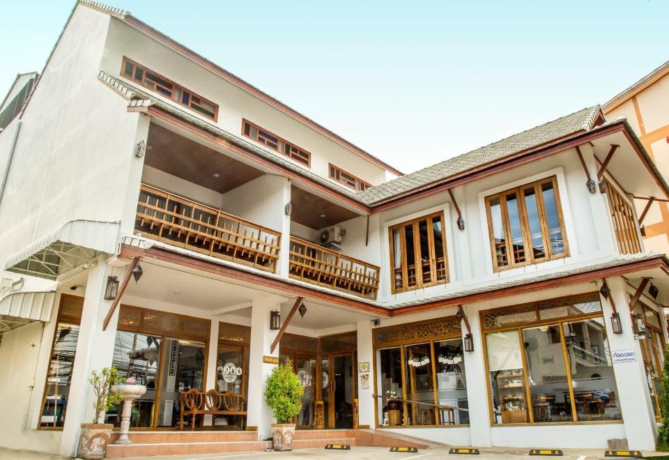 a large white building with multiple floors , balconies , and wooden furniture , situated in a courtyard at The Indigo House Phrae