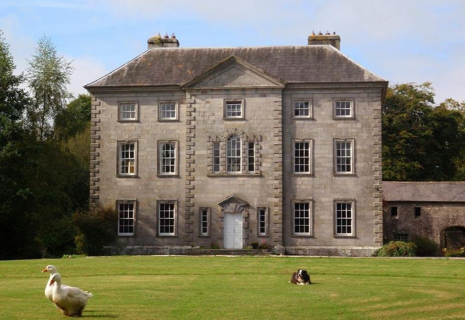 a large stone building with multiple windows and arched windows , surrounded by a grassy lawn and trees at Roundwood House