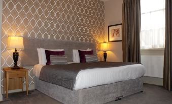 a large bed with a gray headboard and white linens is situated in a room with gray walls at The George at Baldock