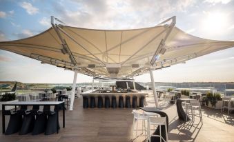 an outdoor bar with a white canopy , tables , chairs , and a view of the ocean at Hilton Garden Inn Silverstone
