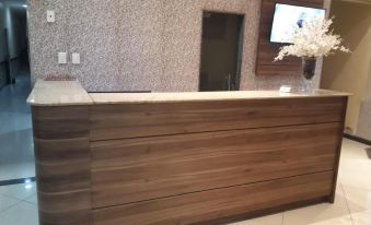 a modern wooden reception desk with a tv and white flowers in front of it at Prime Hotel