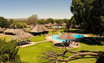 a large resort with a pool surrounded by grassy areas and thatched huts in the background at Midgard