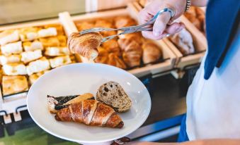 a woman is holding a plate of croissants and bread in a bakery , preparing them for customers at Ibis Como