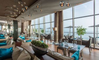 a modern , elegant dining room with large windows offering a view of the ocean , surrounded by comfortable seating and dining tables at Radisson Blu Resort, Gran Canaria