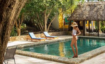 a woman in a white swimsuit stands by the edge of a swimming pool , with lounge chairs and umbrellas nearby at Hacienda San Miguel Yucatan