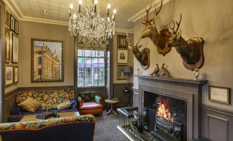 a cozy living room with a fireplace , a couch , and several deer heads mounted on the wall at The Rutland Arms Hotel, Bakewell, Derbyshire