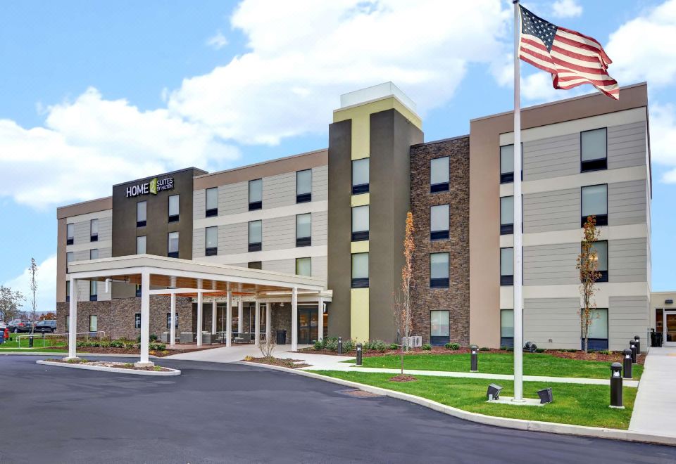 a large hotel building with an american flag on the front , surrounded by grass and trees at Home2 Suites by Hilton Dickson City Scranton