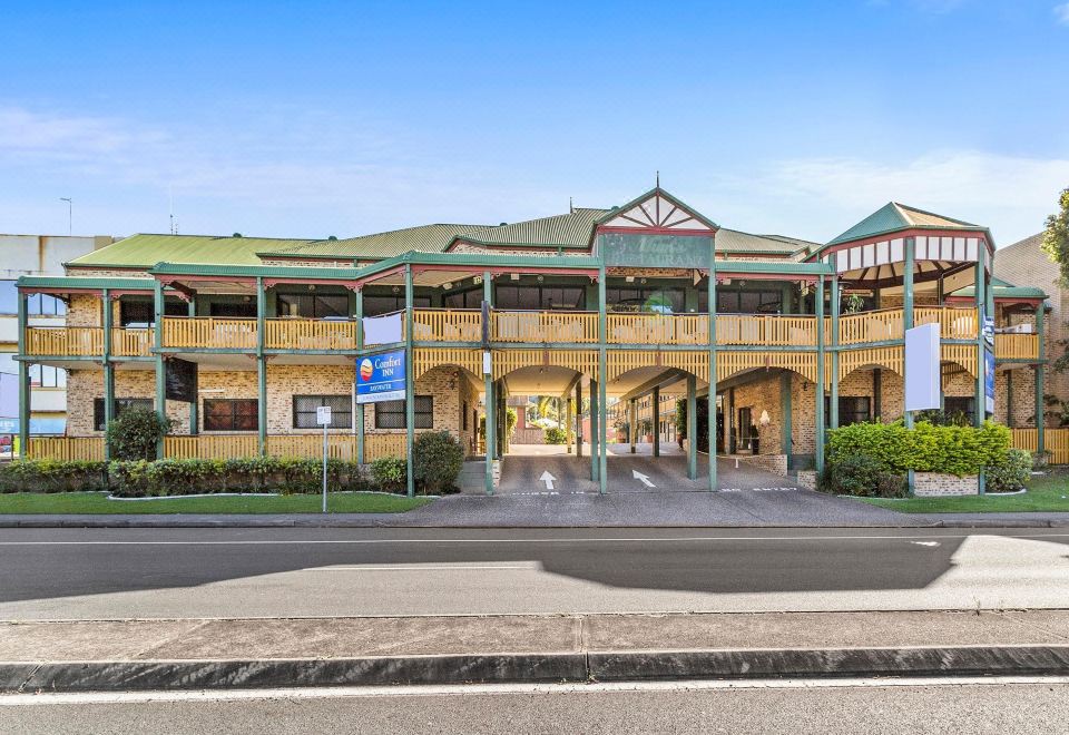 a large building with a green roof and multiple balconies is surrounded by trees and bushes at Bayswater Motel