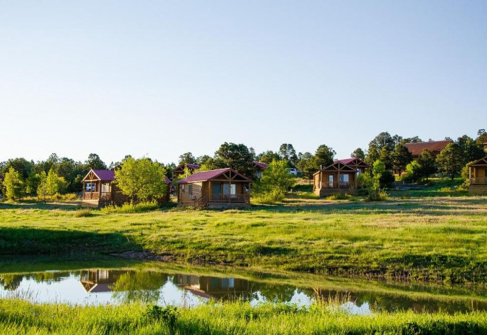 a rural landscape with a group of wooden cabins situated on a grassy field , surrounded by trees and a pond at Zion Mountain Ranch