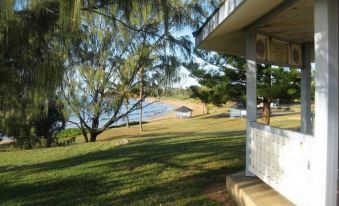 a grassy area with trees and a body of water in the background , creating a serene and peaceful atmosphere at Emu Park Motel