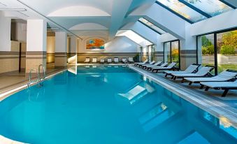 a large , empty indoor swimming pool with blue water and white tiles , surrounded by sun loungers and a skylight at Festa Winter Palace Hotel