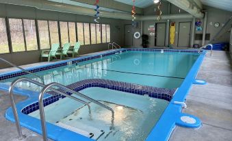 an empty swimming pool with blue water and a diving board , surrounded by chairs and benches at Betsie Riverside Resort