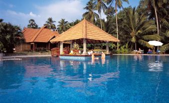 a large swimming pool with a gazebo and palm trees in the background , creating a tropical atmosphere at Poovar Island Resort