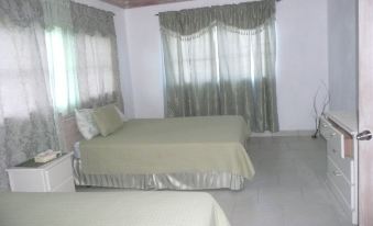 a large bed with a green blanket is in the middle of a room with white walls and curtains at Cottage Cut Villas