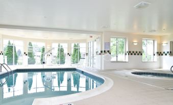 an indoor swimming pool with a hot tub , surrounded by windows that allow natural light to enter at Hilton Garden Inn Wooster