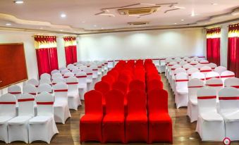 a large , empty banquet hall with white and red drapes , rows of chairs arranged in a semi - circle , and red carpeting at Suva Hotel
