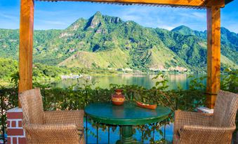 a view of a lake with mountains in the background , taken from a patio with a table and chairs at Eco Hotel Uxlabil Atitlan