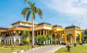 a grand yellow building with multiple turrets , surrounded by palm trees and lush greenery under a clear blue sky at Griya Hotel