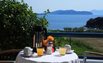 a table with a white tablecloth , two cups of orange juice , and a coffee maker is set up on a balcony overlooking the ocean at Radisson Resort Skiathos
