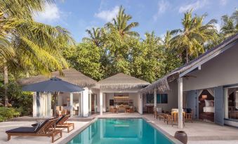 a large pool surrounded by lounge chairs and umbrellas , with palm trees in the background at Raffles Maldives Meradhoo Resort