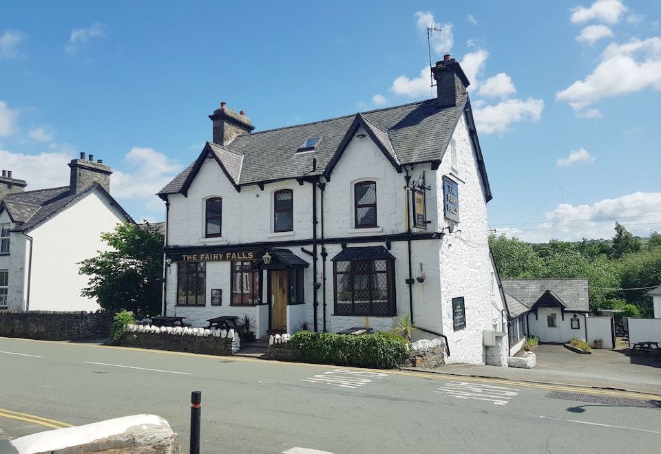 a large white building with a black roof and chimney is situated on the side of a street at The Fairy Falls Hotel