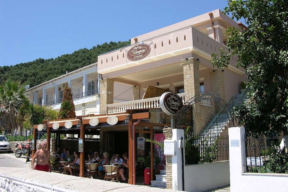 "a white building with a sign that says "" coffee and pastries "" is surrounded by trees , with people sitting outside" at Utopia