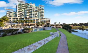 a large , modern apartment building with a green lawn and walkway , situated near a body of water at Pelican Waters Resort