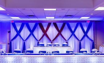 a banquet hall with a stage set up for an event , featuring blue and white drapes and a long table at Holiday Inn Weirton - Steubenville Area