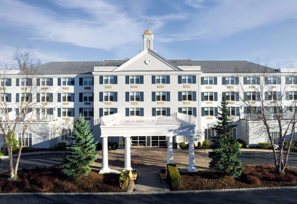 a large white hotel building with a blue roof , surrounded by trees and set against a clear sky at Somerset Hills Hotel, Tapestry Collection by Hilton