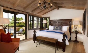 a bedroom with a large bed , wooden headboard , and white linens is shown with an open door leading to an outdoor patio at Rancho Valencia Resort and Spa