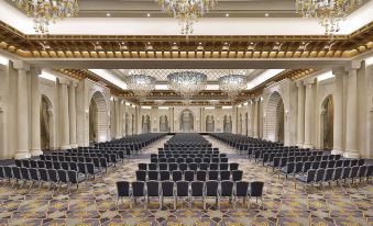 a large , ornate conference room with rows of chairs arranged in a symmetrical fashion , under a shiny ceiling and decorated with chandeliers at Hilton Suites Makkah