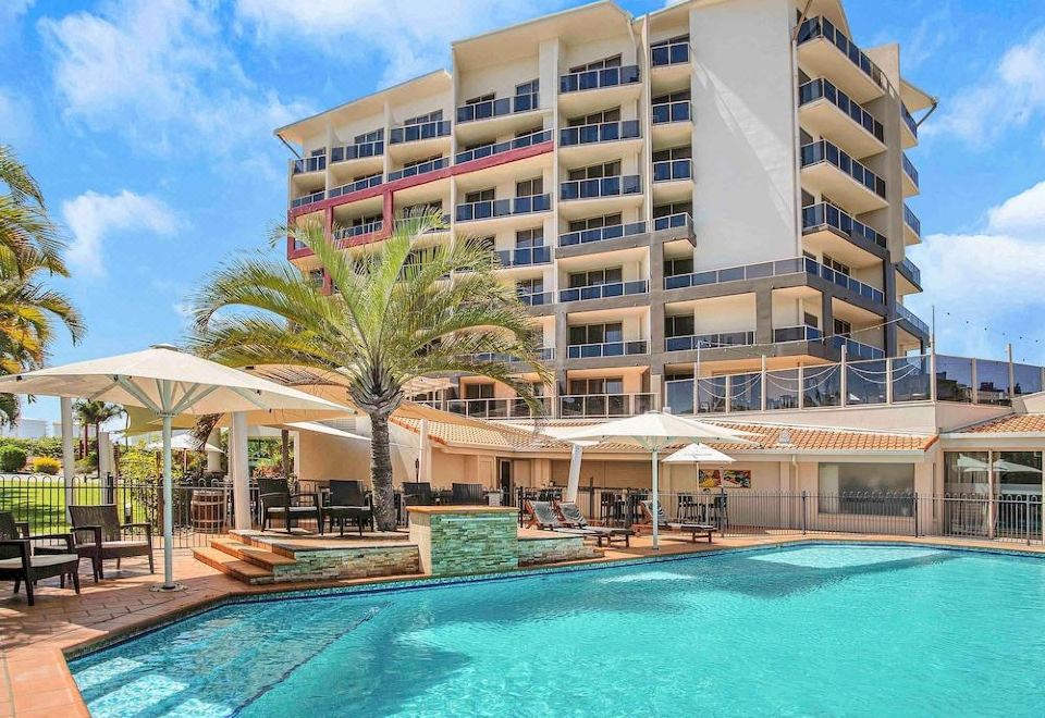 a large swimming pool with umbrellas and lounge chairs is located in front of a tall building at Mantra Mackay