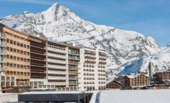 a snow - covered mountain with a ski resort in the background , and a large building with multiple floors at Langley Hotel Tignes 2100